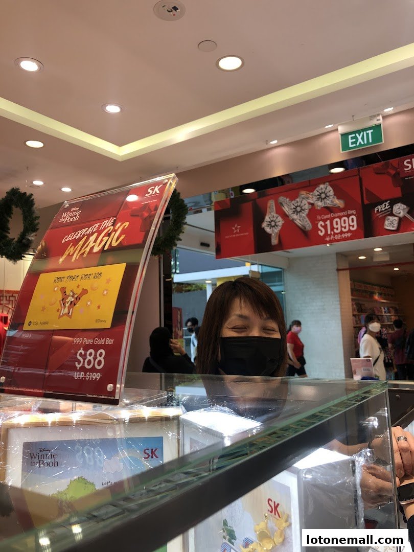 A woman wearing a mask smiles behind a display of jewelry and gold bars.
