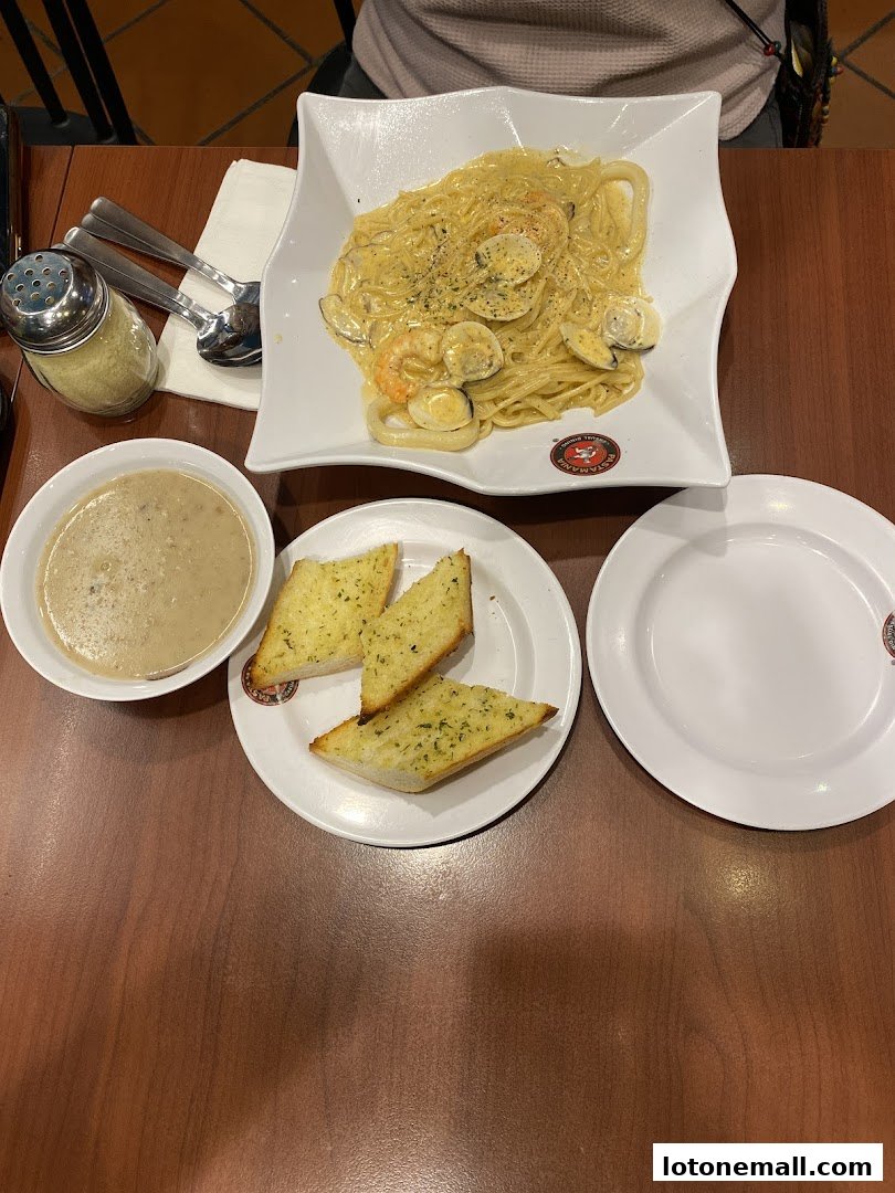 A table setting with a creamy seafood pasta, garlic bread, and a bowl of soup.