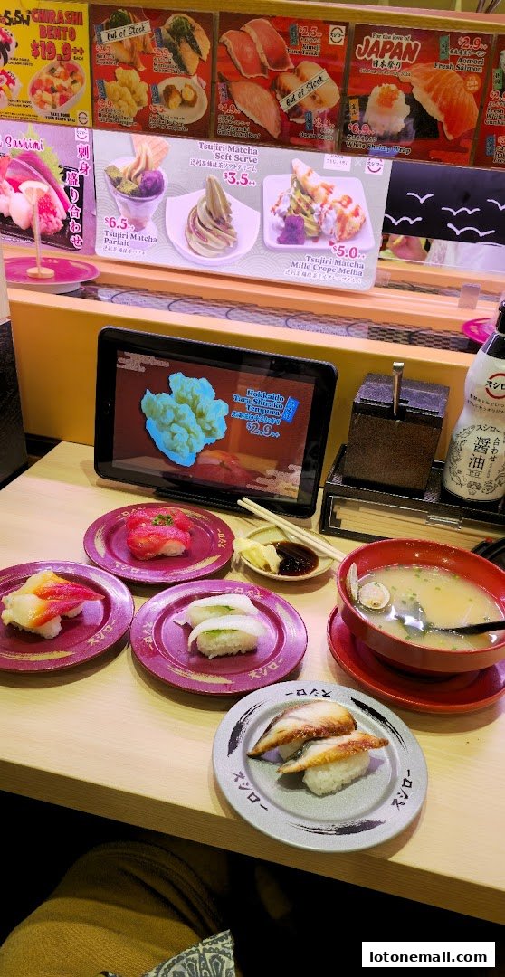 A table at Sushiro Lot One with various sushi plates, a bowl of soup, and a tablet displaying food.