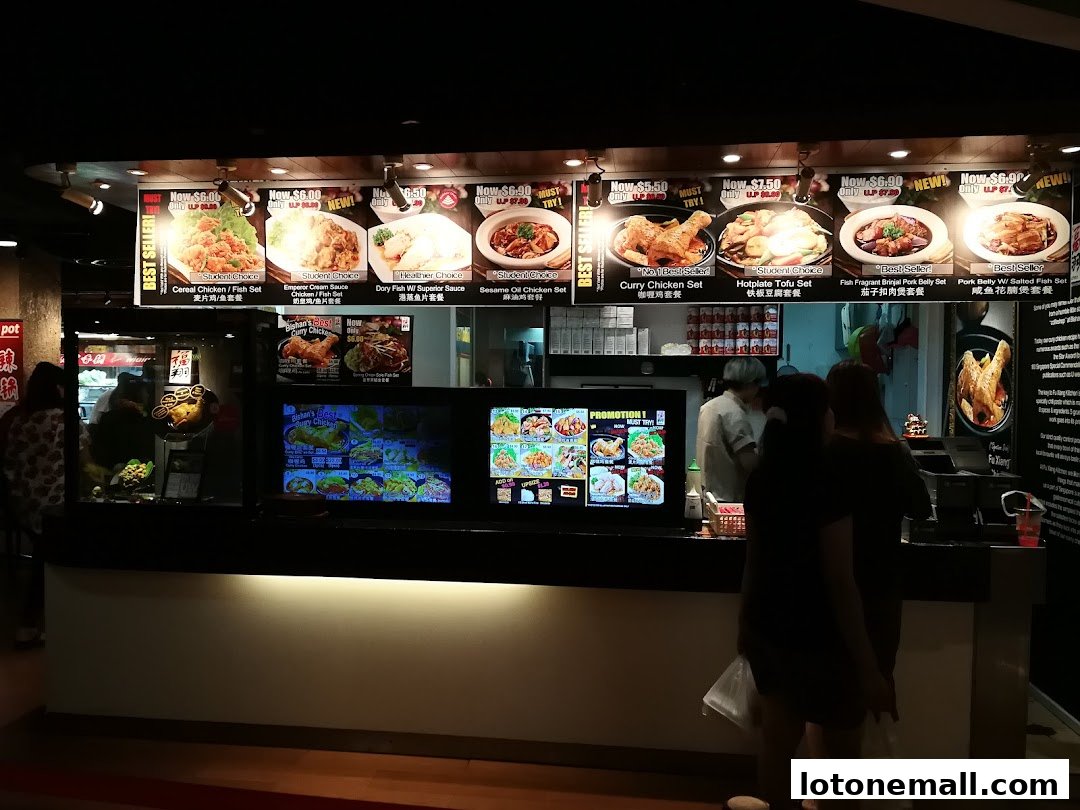A food court stall with illuminated menu boards displaying various meal sets and dishes.