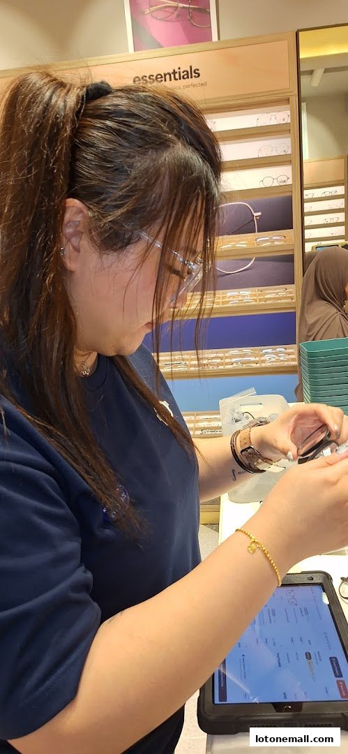 A woman in a blue shirt is examining eyeglasses at a counter with a tablet.