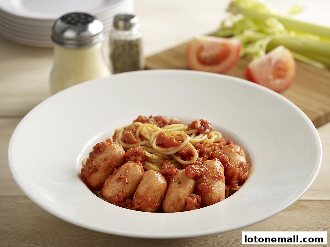 A close-up of a pasta dish with sausages and tomato sauce, garnished with celery and tomatoes.