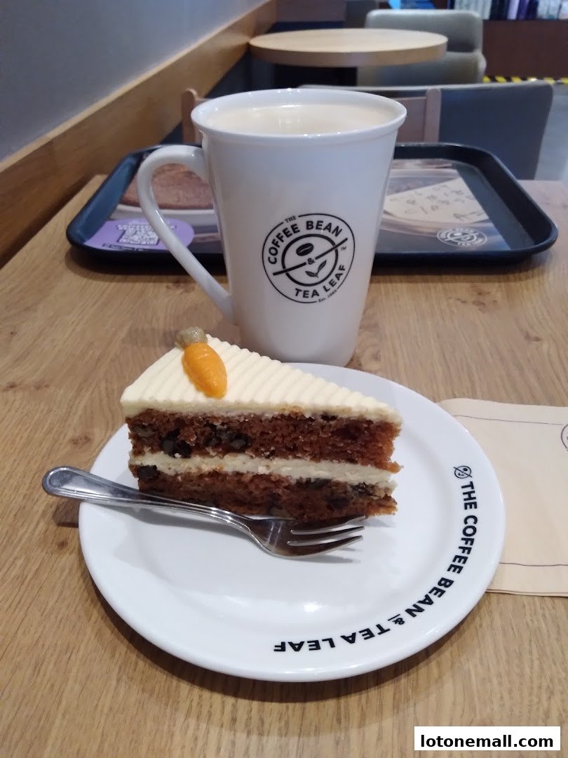 A slice of carrot cake and a mug of coffee on a wooden table.