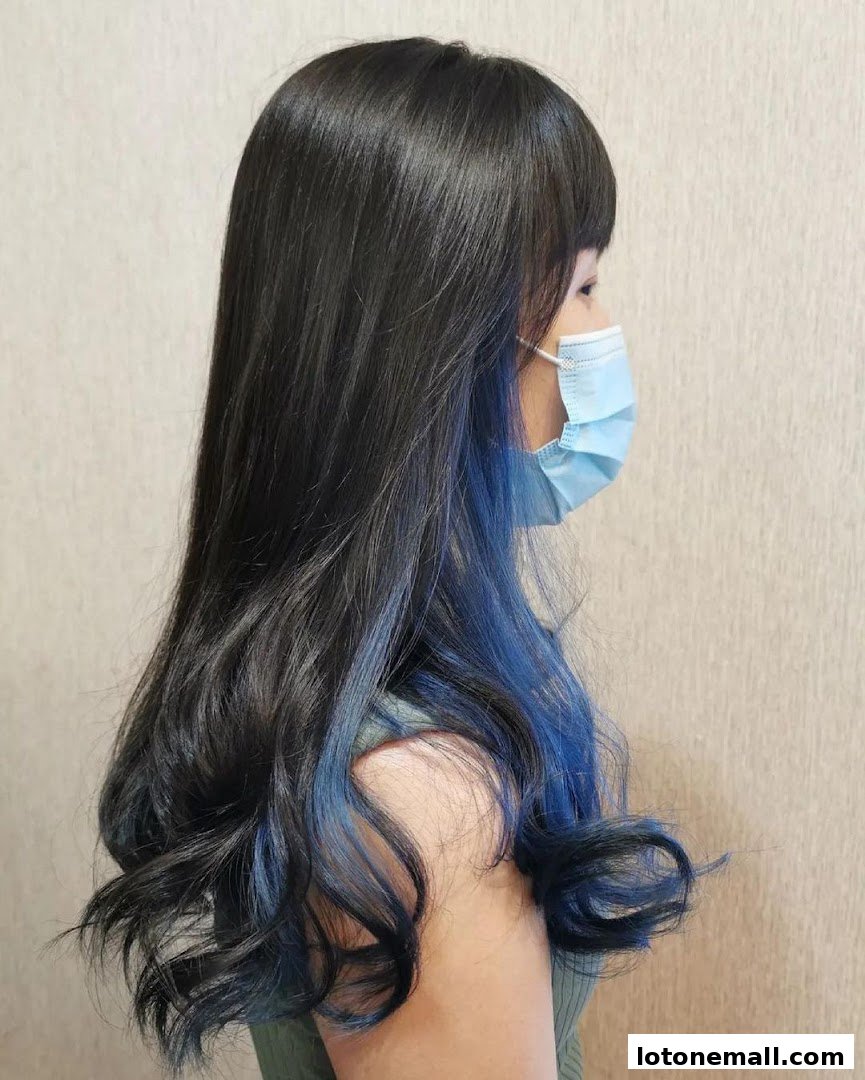 A woman with long black hair with blue highlights, wearing a face mask.