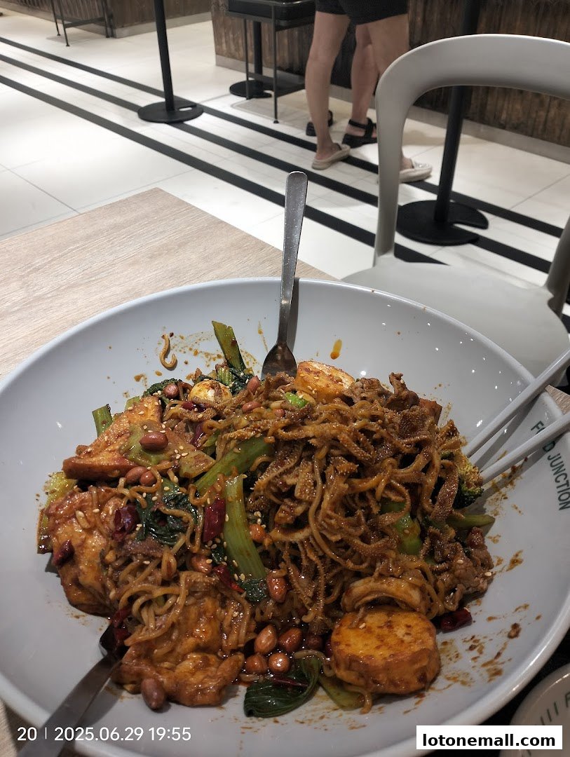 A close-up of a large bowl of spicy noodles with various ingredients, including vegetables and peanuts.