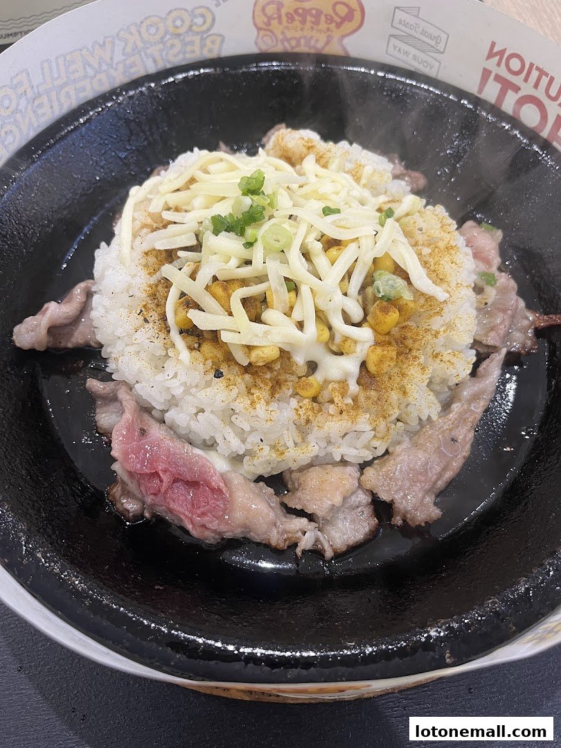 A sizzling hot plate of rice with beef, cheese, and corn, garnished with spring onions.
