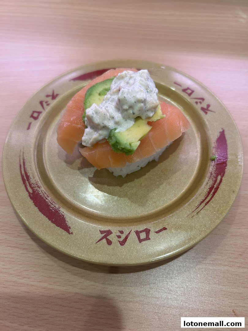 A plate of salmon sushi with avocado and a creamy topping on a wooden table.