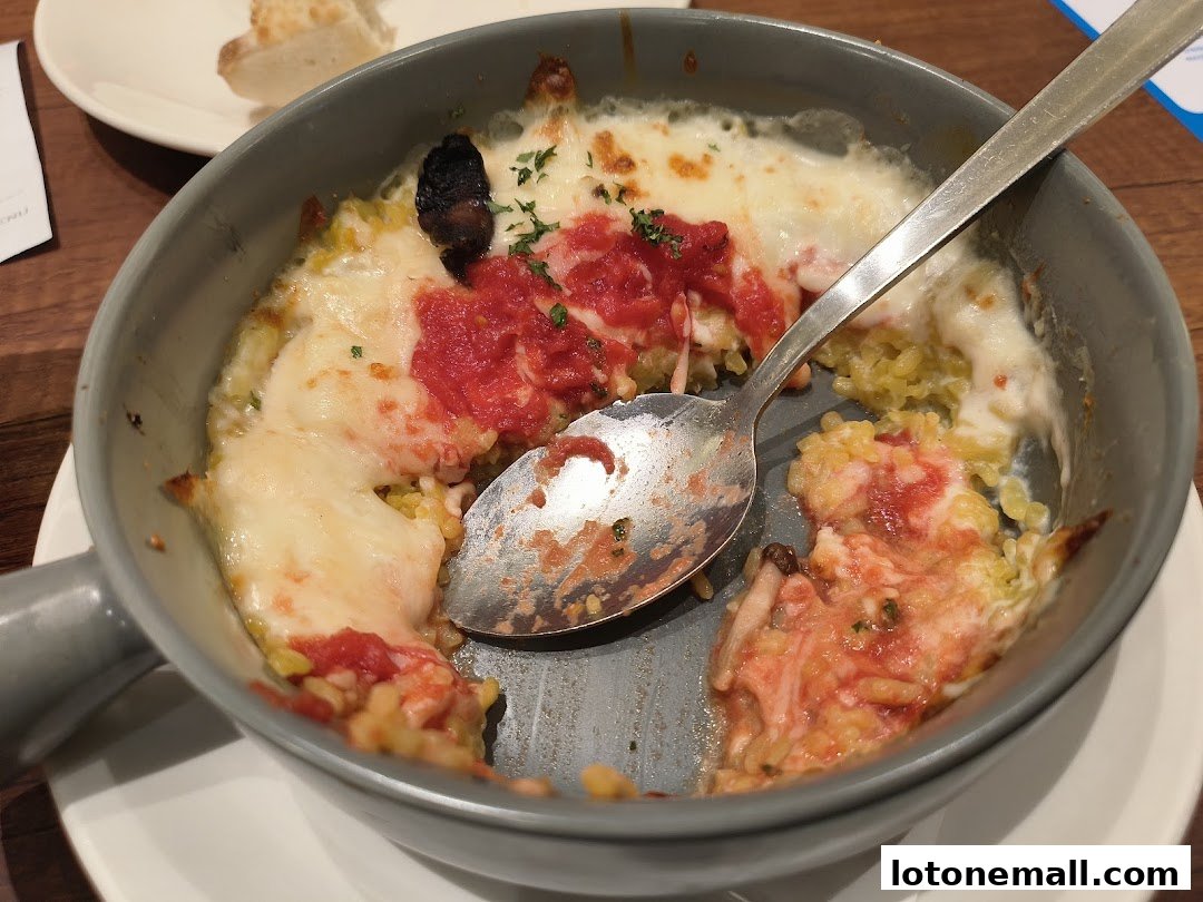 A close-up of a cheesy baked dish with tomato sauce and rice, partially eaten.