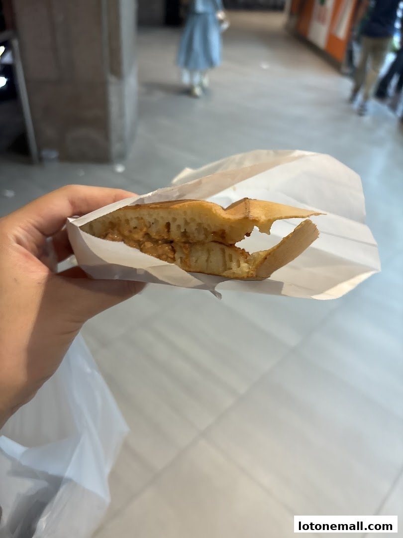A hand holds a peanut-filled pancake in a white paper bag.