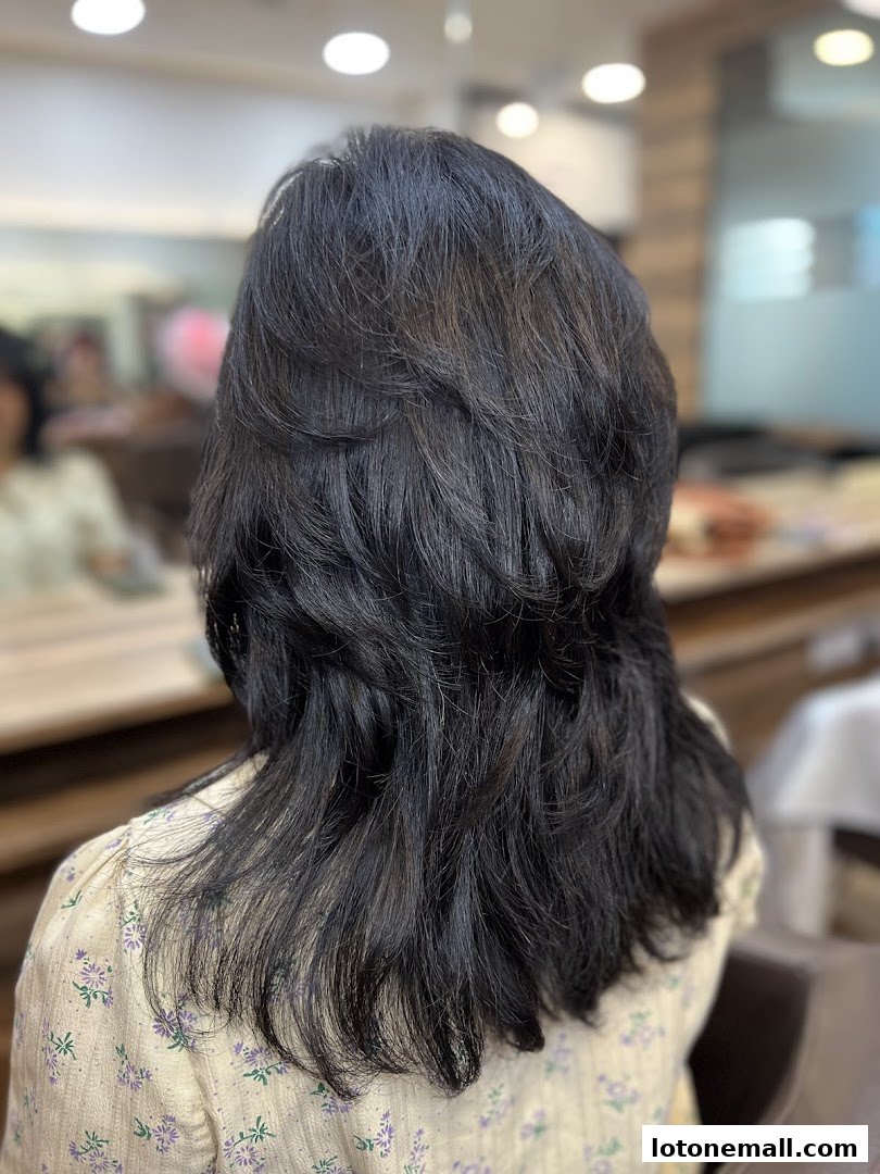 A person with dark, layered hair is shown from behind in a salon.