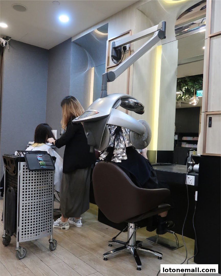 A hair salon interior with a client receiving hair treatment under a dryer.