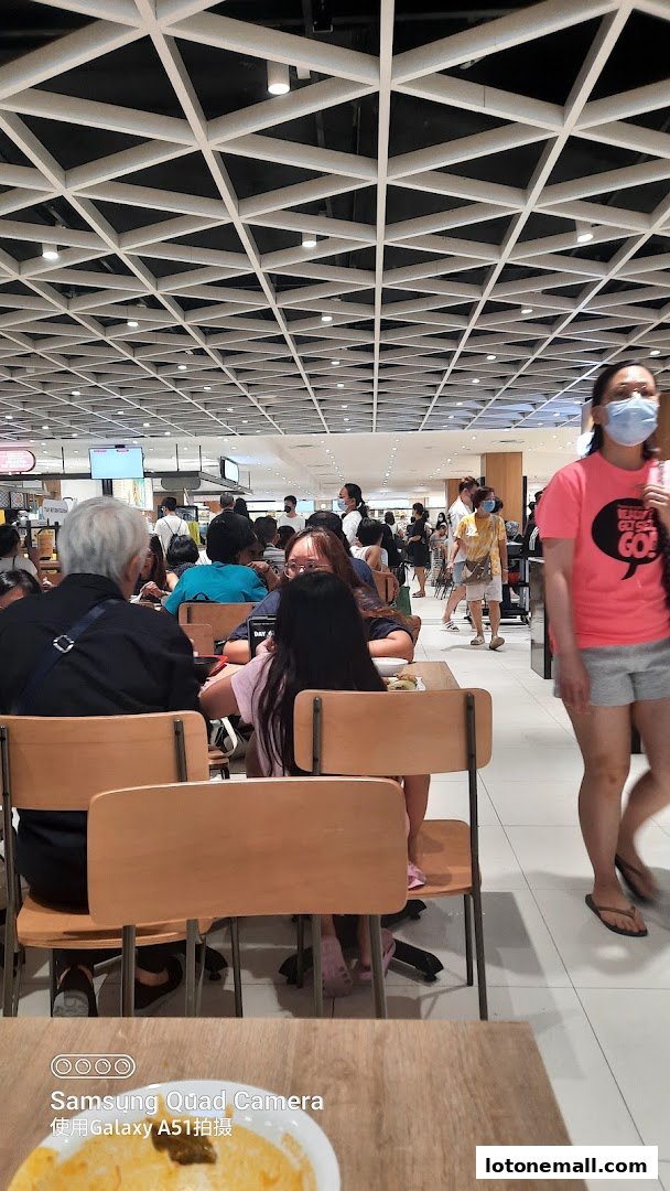 People dining at tables in a busy food court with a modern geometric ceiling.