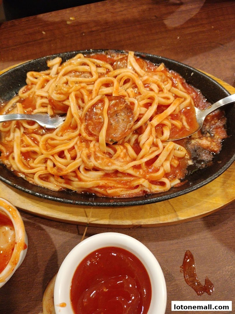 A sizzling plate of spaghetti with meatballs and a side of ketchup.