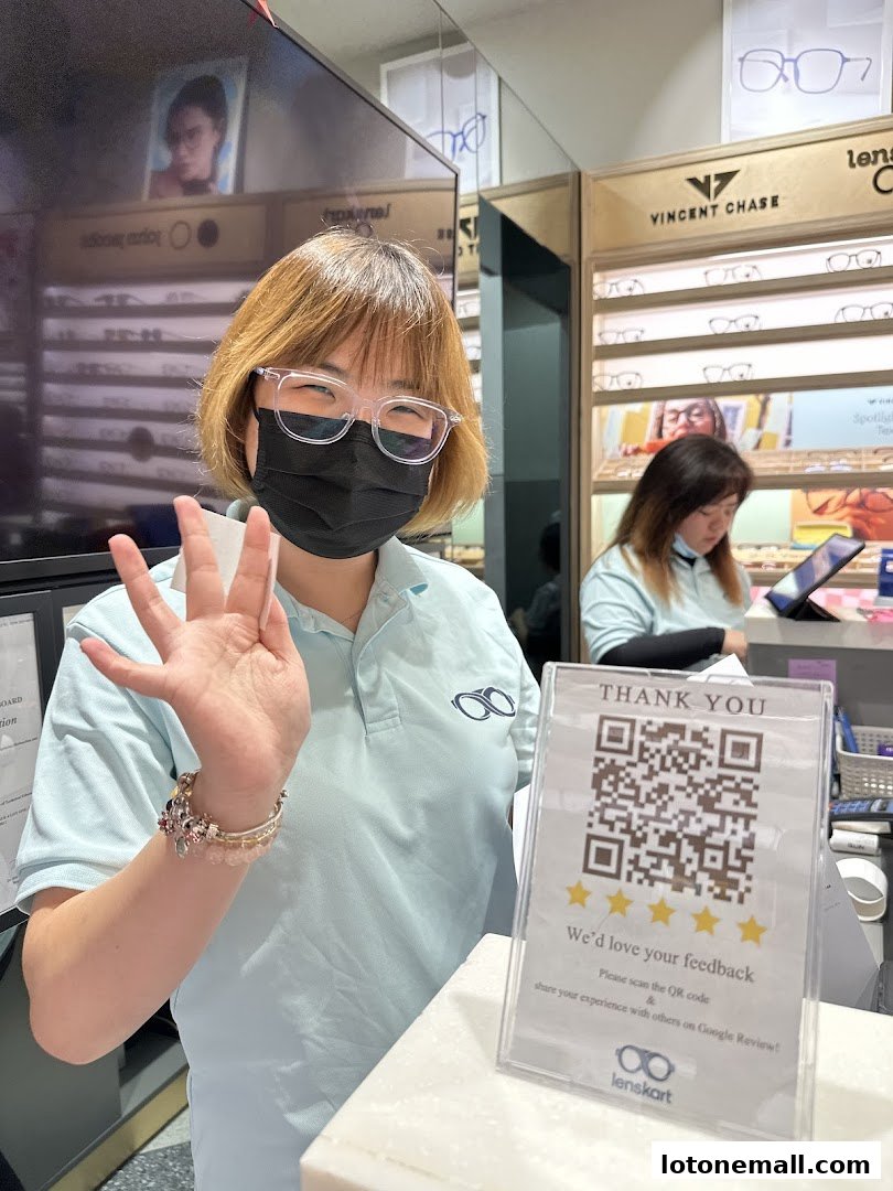 A Lenskart employee waves while a customer browses glasses in the background.