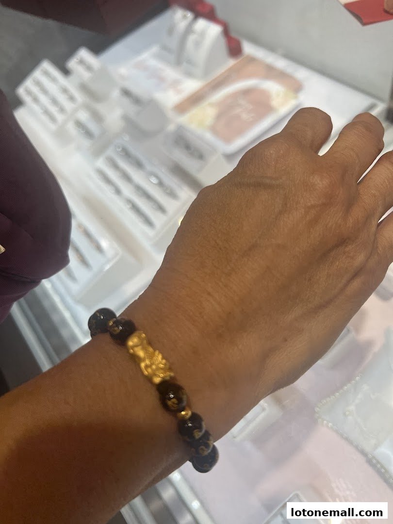 A person's wrist displays a gold and bead bracelet with a Pixiu charm.