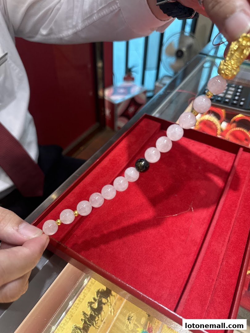 A person is holding a rose quartz beaded bracelet with gold accents and a black bead.