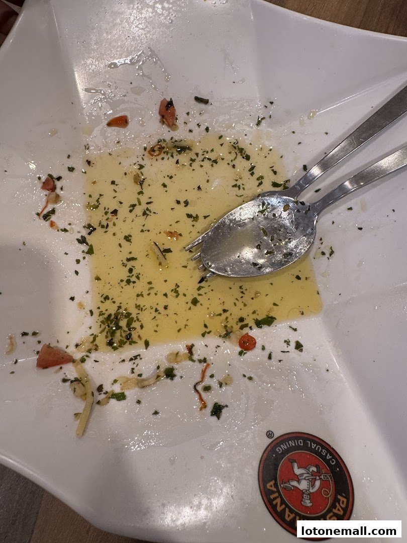 A dirty plate with leftover pasta, herbs, and cutlery after a meal.
