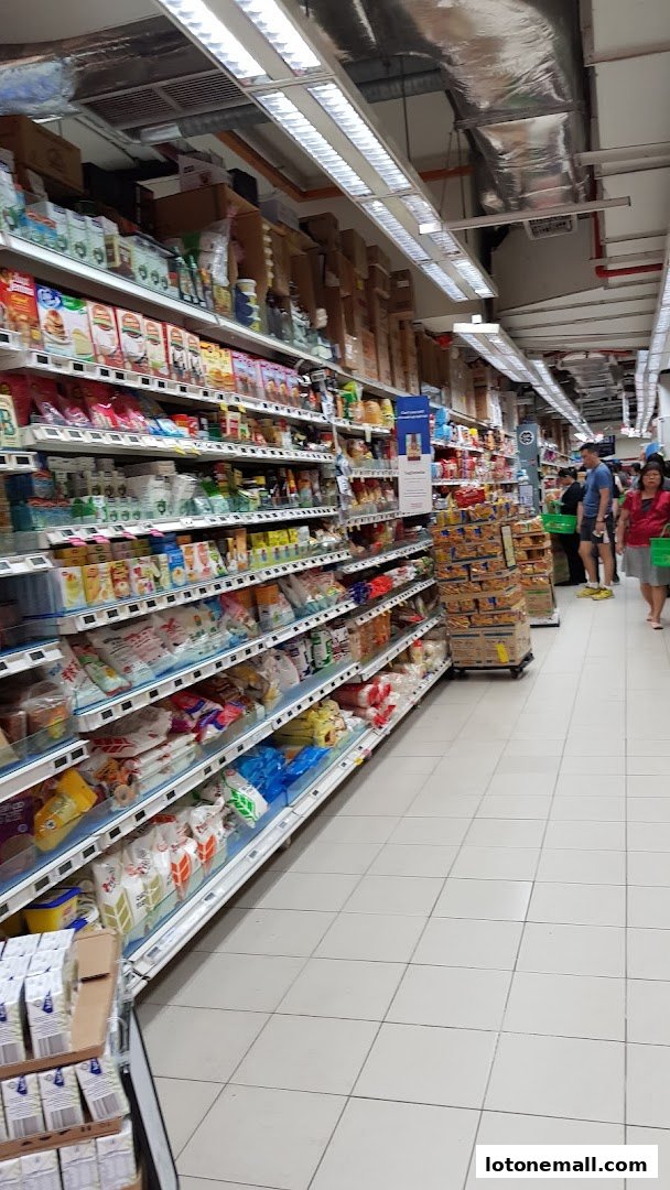 Aisle of a supermarket with shelves stocked with various food products and shoppers.
