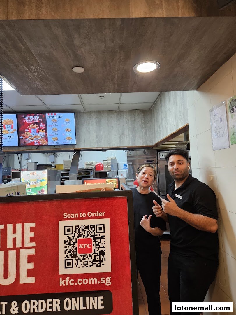Two KFC staff members stand near a counter with a QR code for ordering.