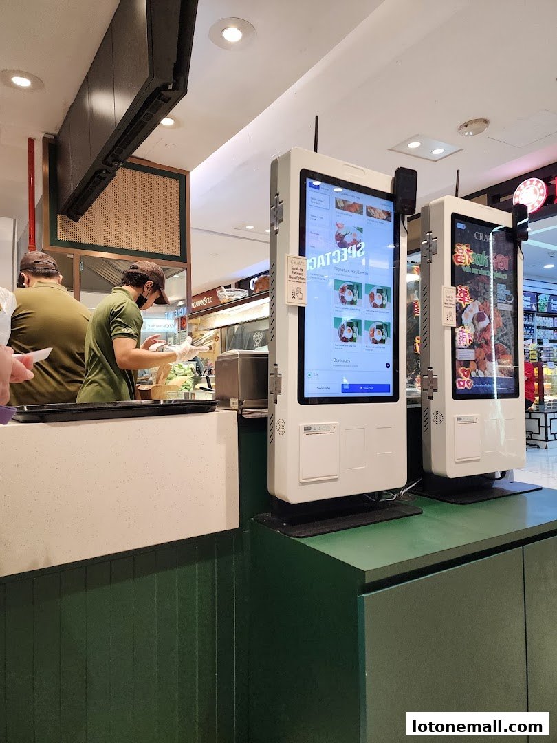 Staff preparing food behind a counter with digital ordering kiosks.