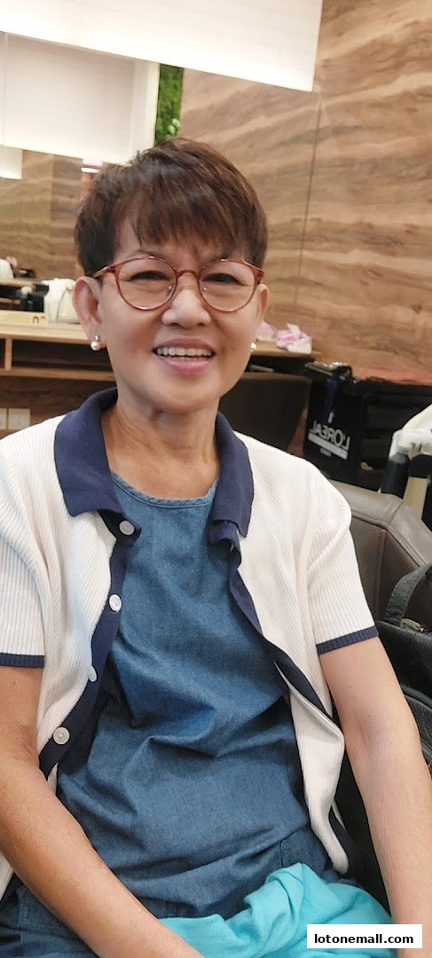 A smiling woman with short brown hair and glasses sits in a salon chair.
