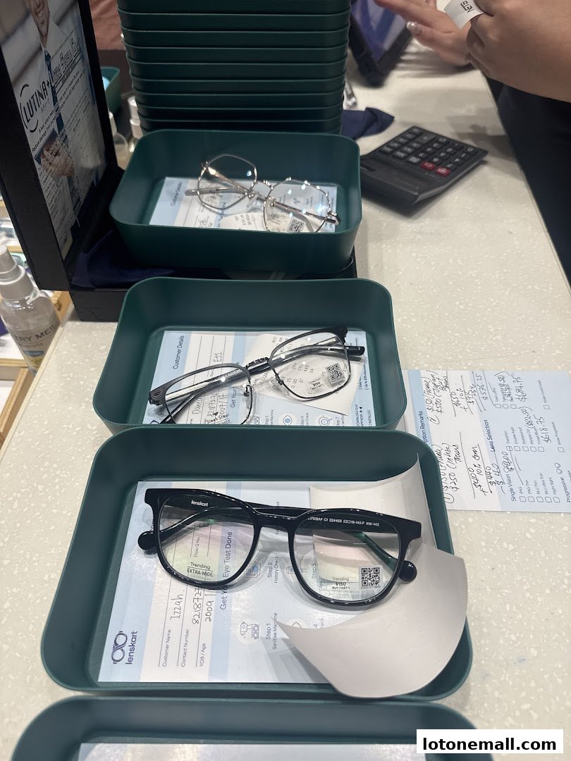 A display of various eyeglasses in trays at Lenskart, with a calculator and customer forms visible.