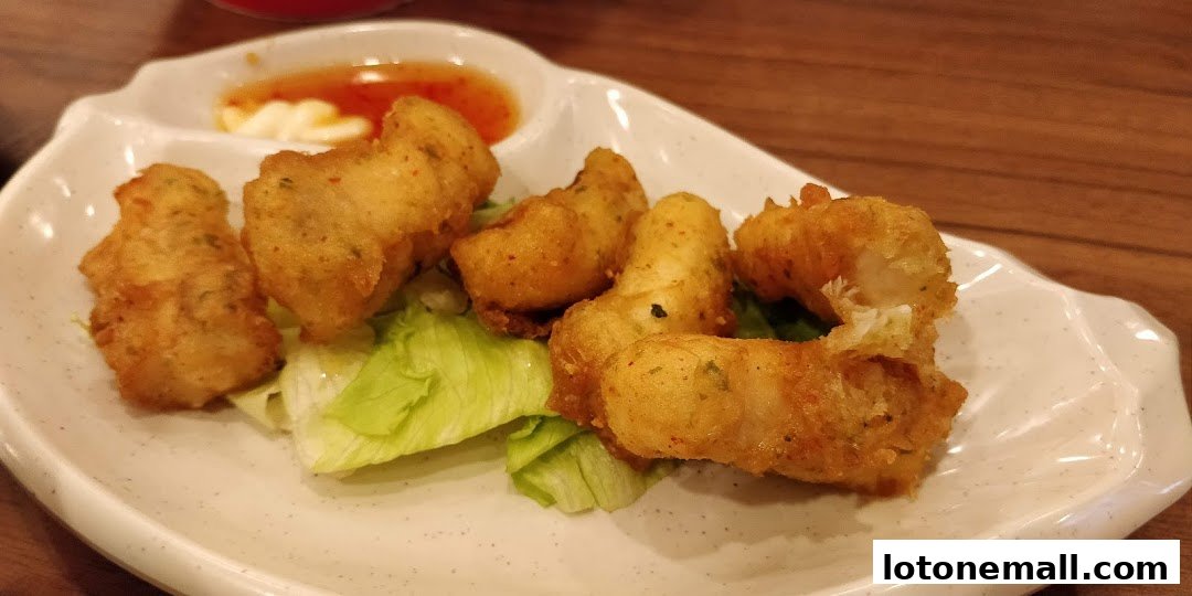 Crispy fried fish pieces served with dipping sauces and lettuce on a white plate.