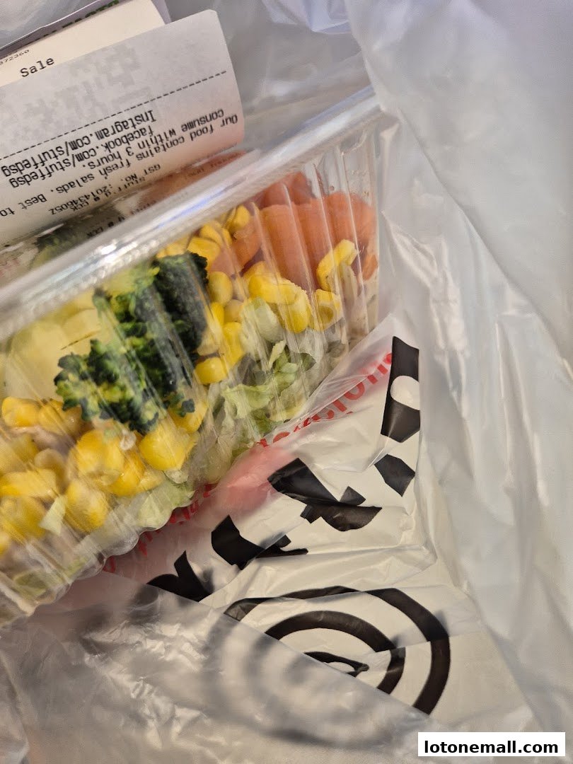 A clear plastic container filled with a fresh salad, placed inside a branded shopping bag.
