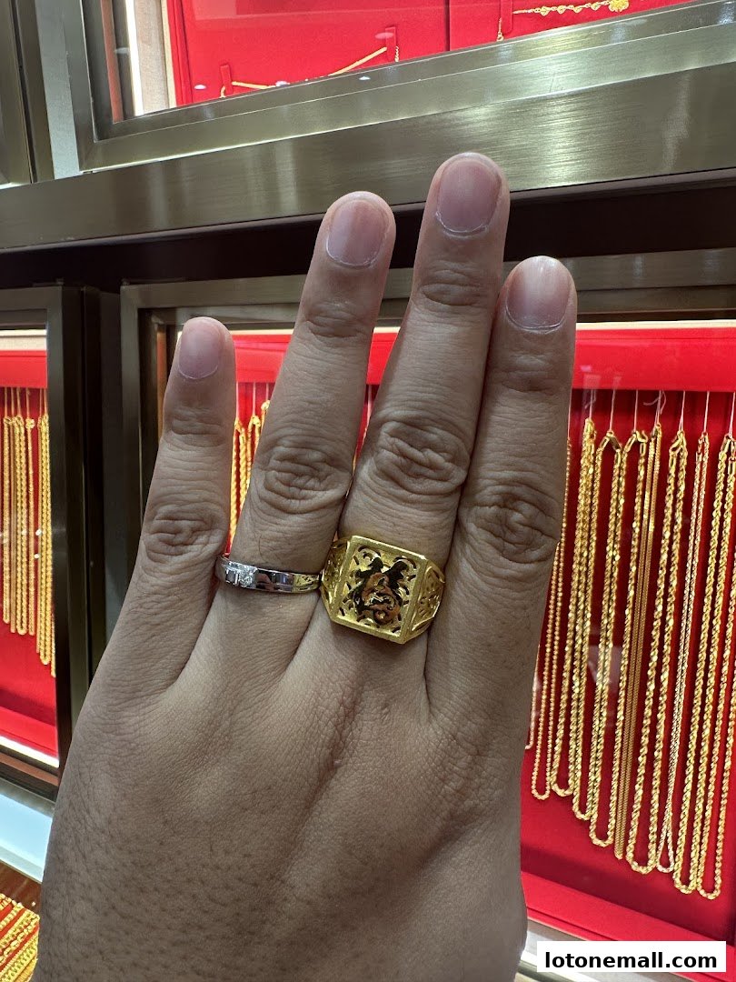 A hand wearing a gold ring with a Chinese character and a diamond ring, with gold necklaces displayed in the background.