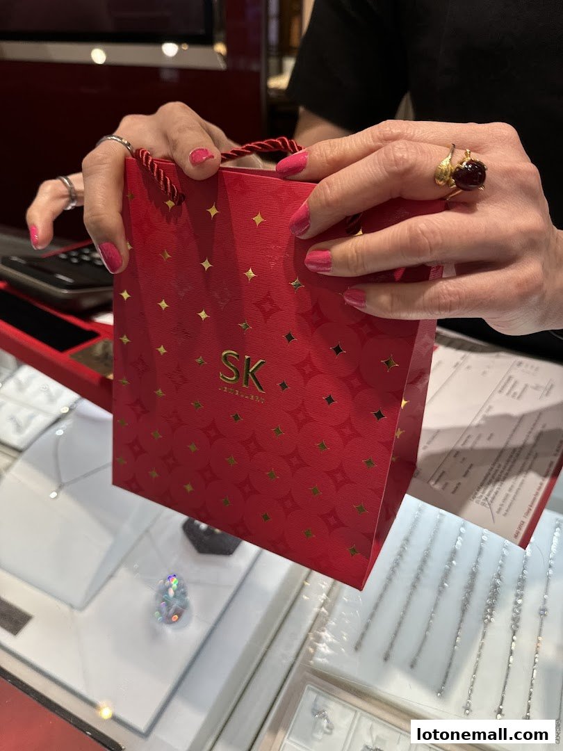 A person holds a red SK Jewellery gift bag with gold stars, showcasing a large ring.