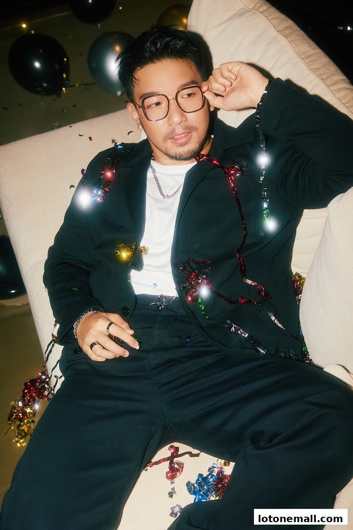 A man wearing glasses and a suit jacket decorated with festive lights and confetti.