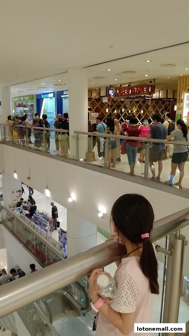 People queuing at shops on different levels of a mall, with a girl in the foreground.