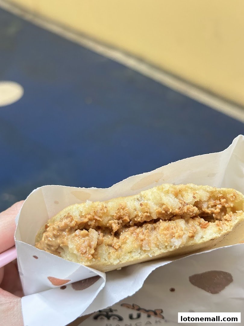 A close-up of a pancake filled with peanut butter, held in a paper wrapper.