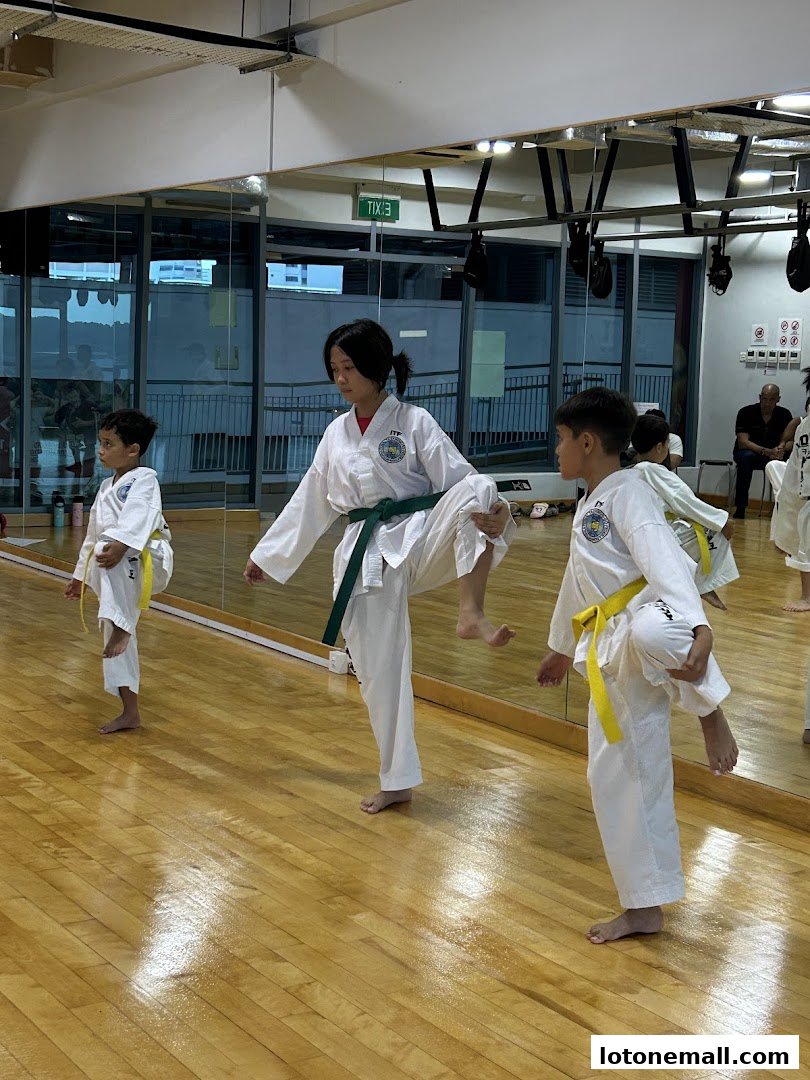 Children practicing Taekwondo kicks in a studio with mirrors and wooden floors.