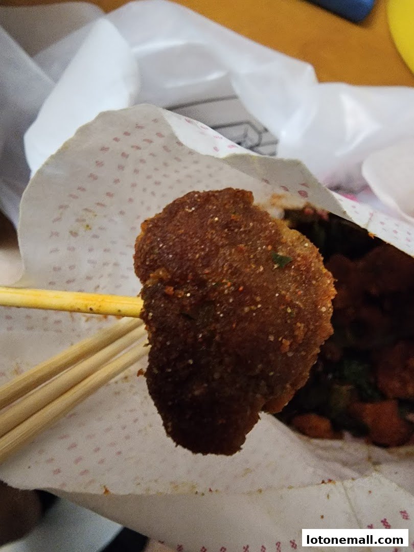 A close-up of a piece of fried chicken on a skewer, seasoned with spices.