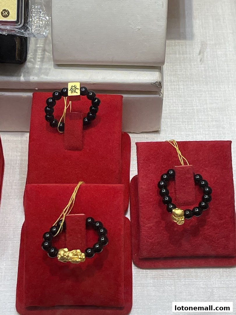 Close-up of black beaded bracelets with gold charms, displayed on red velvet stands.