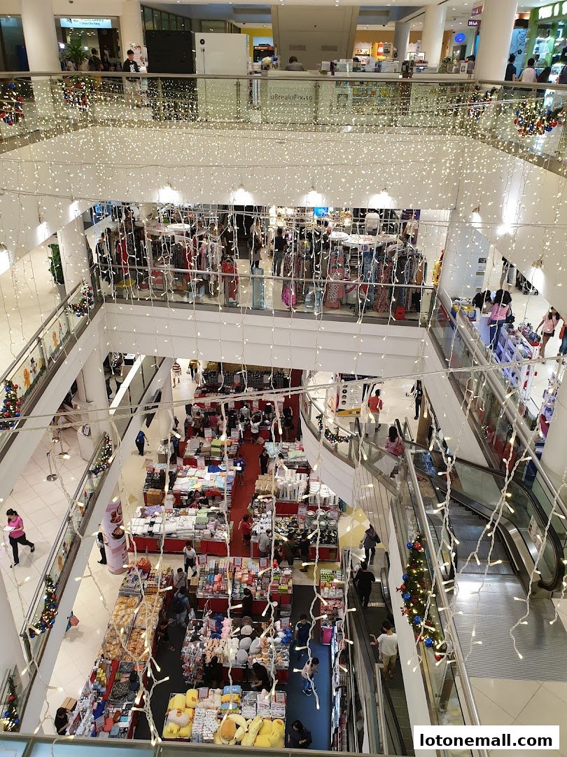 A multi-level shopping mall interior decorated with festive lights and filled with various retail stalls.