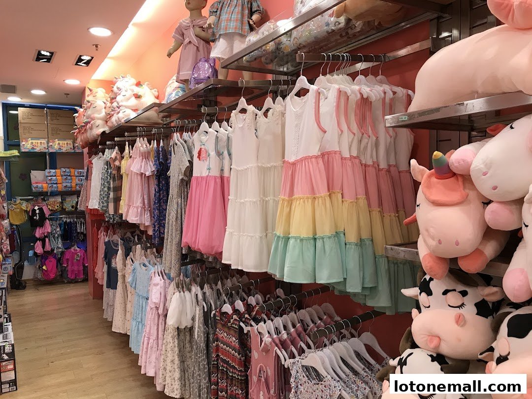 A brightly lit shop interior displaying colorful children's dresses and plush unicorn and cow toys.