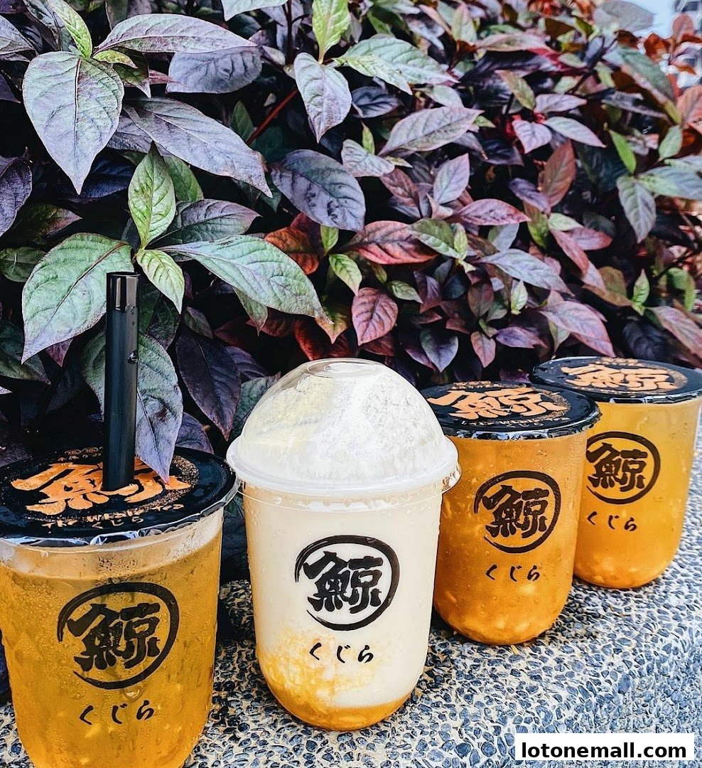 Four bubble tea drinks with the brand logo are displayed in front of lush foliage.
