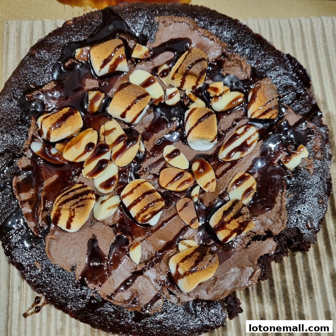A close-up of a chocolate dessert pizza topped with marshmallows, almonds, and chocolate sauce.