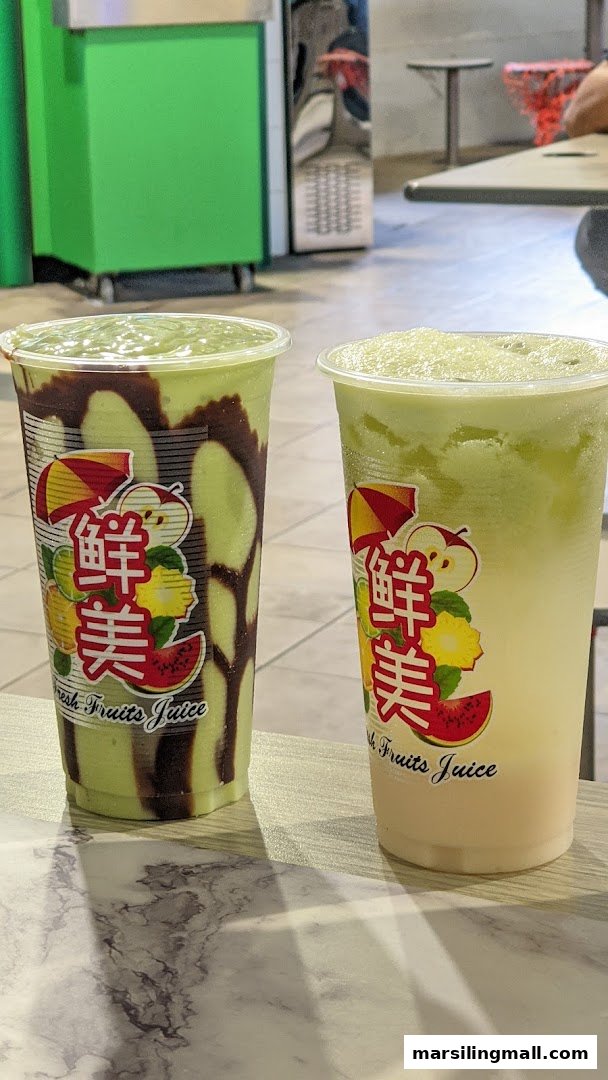 Two refreshing green-colored fruit juice drinks, one with chocolate drizzle, on a marble-patterned table.