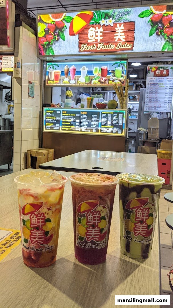 Three colorful fresh fruit juice drinks on a table, with the juice bar counter and menu visible in the background.
