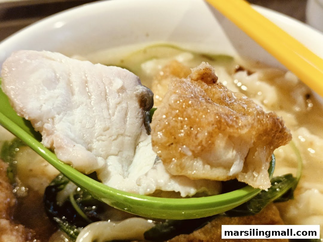 Close-up of a spoonful of fresh and fried fish slices from a bowl of fish soup.