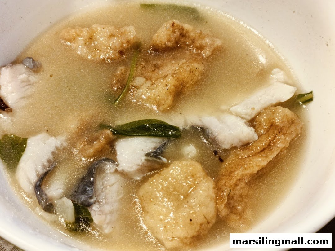 A close-up of a comforting bowl of fish soup with tender fish slices, fried fish skin, and green herbs.