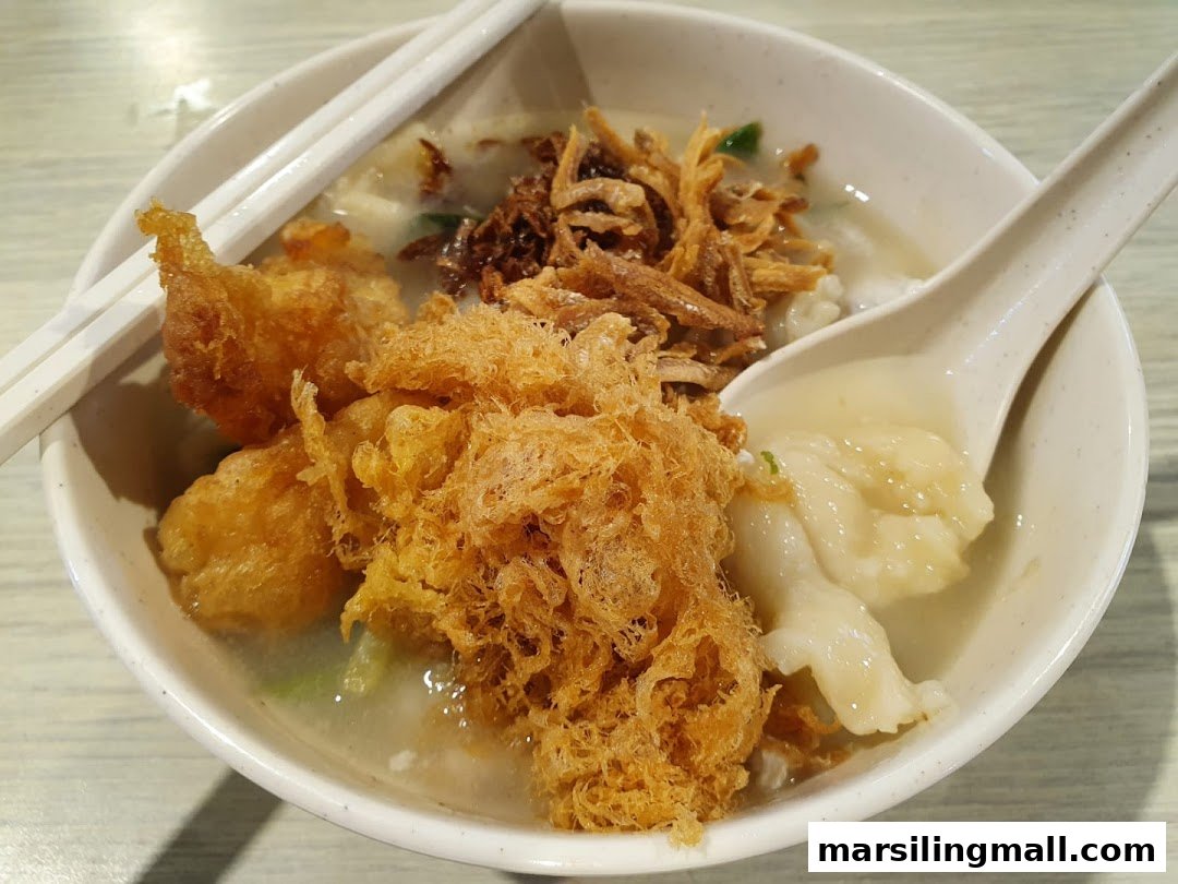 A close-up of a hearty bowl of Ah Yi's handmade noodle fish soup with crispy toppings and dumplings.