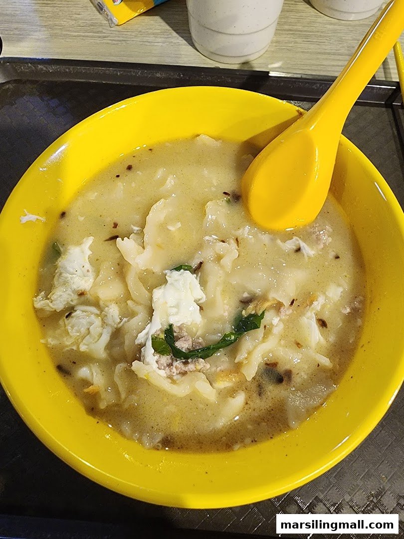 A vibrant yellow bowl filled with Ah Yi Handmade Noodle Fish Soup, featuring noodles, minced meat, and egg.