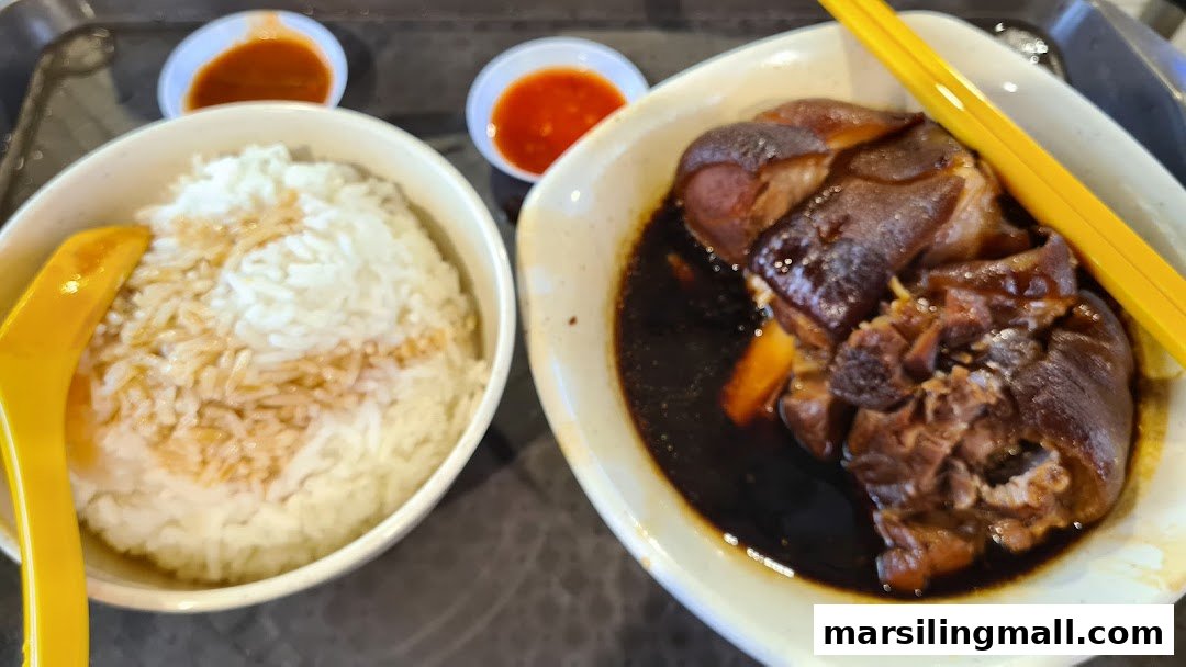 A close-up of a hearty meal featuring braised pork trotters with rice and chili sauce.