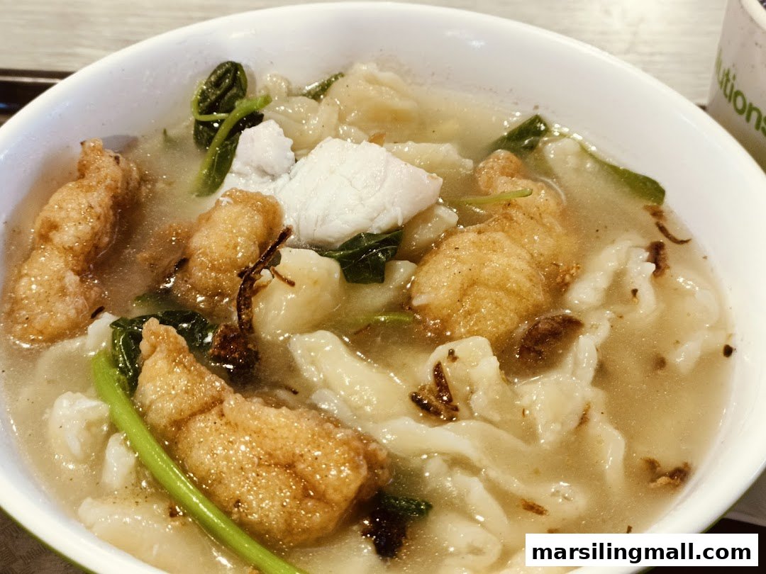 A close-up of a bowl of Ah Yi Handmade Noodle Fish Soup with fried and fresh fish slices.