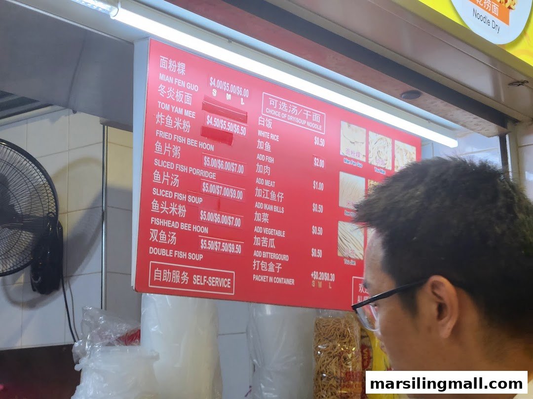 A red menu board displaying various noodle and fish soup dishes with prices, viewed by a customer.