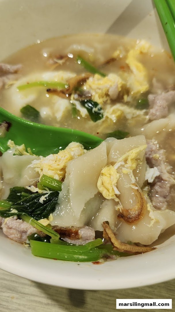 A close-up of a comforting bowl of handmade noodles with minced meat, vegetables, and egg in a savory broth.